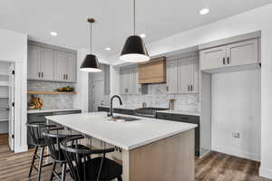 Dual tone kitchen featuring a breakfast bar area, light stone counters, dual tone cabinets, a center island with sink, and pendant lighting