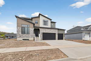 Modern home featuring stone siding, driveway, and a garage