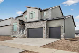 Modern home featuring concrete driveway, stone siding, and an attached garage