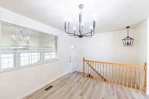 Unfurnished dining area with a chandelier and light wood-type flooring