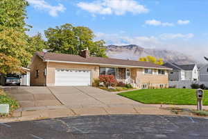 Ranch-style home with brick siding, a mountain view, a chimney, an attached garage, and driveway