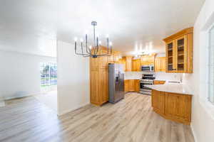 Kitchen featuring stainless steel appliances, glass insert cabinets, a peninsula, hanging lights, and light wood-style floors