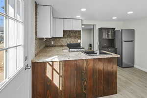 Kitchen with a peninsula, freestanding refrigerator, tasteful backsplash, light stone counters, and light wood-style flooring
