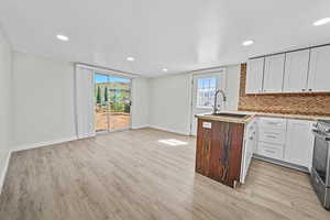 Kitchen with white cabinets, a peninsula, tasteful backsplash, light wood finished floors, and stainless steel range