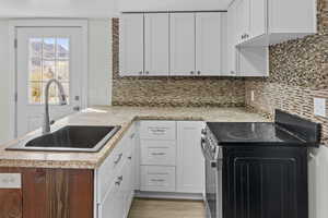 Kitchen featuring white cabinets, a peninsula, electric range, light countertops, and decorative backsplash