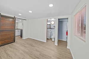 Unfurnished bedroom featuring a barn door, ensuite bathroom, a spacious closet, recessed lighting, and light wood finished floors