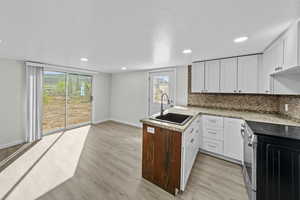 Kitchen featuring stainless steel electric range oven, a peninsula, backsplash, light wood-style flooring, and recessed lighting