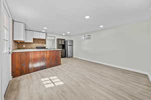 Kitchen with light wood-style floors, freestanding refrigerator, a peninsula, open floor plan, and decorative backsplash