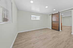 Unfurnished bedroom with a barn door, light wood-style floors, and recessed lighting