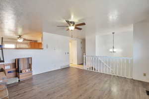 Unfurnished living room featuring ceiling fan, a textured ceiling, wood finished floors, and suspended lighting