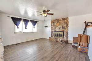 Unfurnished living room with ceiling fan, a textured ceiling, dark wood finished floors, and a stone fireplace