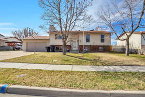 Split foyer home with a garage, concrete driveway, a chimney, and brick siding