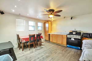 Kitchen with stainless steel gas stove, light countertops, light wood-style floors, black microwave, and ceiling fan