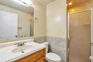 Full bath featuring vanity, a shower stall, tile walls, ornamental molding, and a wainscoted wall