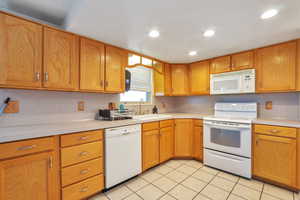 Kitchen featuring white appliances, light countertops, light tile patterned flooring, wood finish cabinets, and recessed lighting