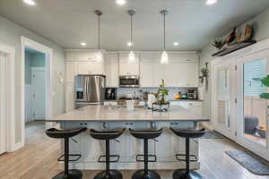 Kitchen with white cabinets, stainless steel appliances, light wood finished floors, and a spacious island