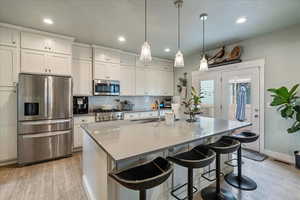Kitchen with stainless steel appliances, light wood-style flooring, white cabinetry, and a kitchen breakfast bar