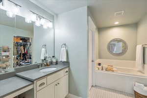 Bathroom featuring vanity, a textured ceiling, a garden tub, recessed lighting, and a walk in closet