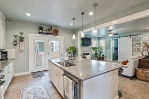 Kitchen featuring a barn door, open floor plan, white cabinetry, an island with sink, and a fireplace