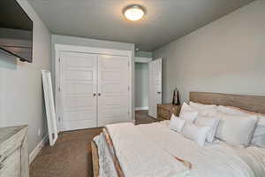 Bedroom with a closet, dark colored carpet, and a textured ceiling