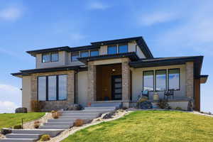 Prairie-style home featuring stucco siding, stone siding, a front yard, and covered porch