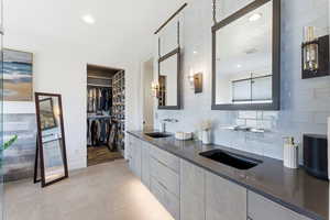 Full bathroom featuring light tile patterned flooring, decorative backsplash, double vanity, a walk in closet, and recessed lighting