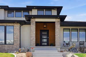 Doorway to property featuring stucco siding, covered porch, and stone siding