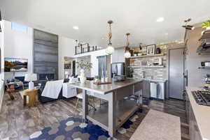 Kitchen with open shelves, stainless steel appliances, dark wood-type flooring, pendant lighting, and open floor plan
