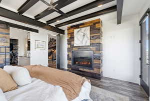 Bedroom featuring a barn door, a stone fireplace, beamed ceiling, and wood finished floors