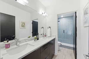 Full bathroom with double vanity, a stall shower, and light wood-style floors