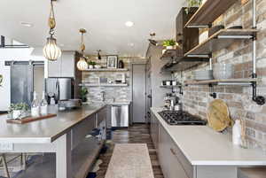 Kitchen with open shelves, stainless steel appliances, hanging light fixtures, a barn door, and dark wood finished floors