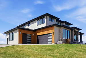 Contemporary home featuring a front lawn, stucco siding, an attached garage, and driveway