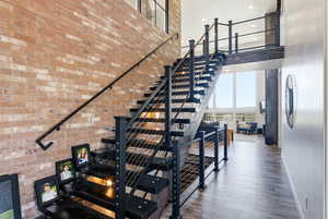 Staircase featuring a high ceiling, wood finished floors, and brick wall