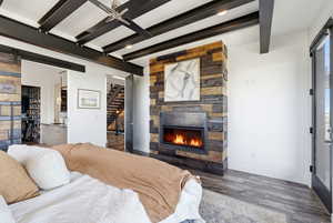 Bedroom with a barn door, a fireplace, beamed ceiling, and wood finished floors