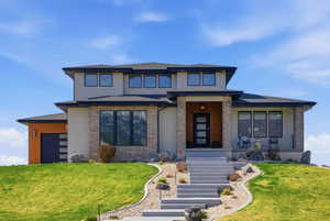 Prairie-style home with stucco siding, roof with shingles, a front lawn, an attached garage, and stone siding