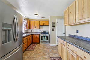 Kitchen featuring stainless steel appliances, dark countertops, stone finish flooring, and a textured ceiling