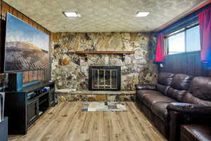 Living room featuring light wood-type flooring, a stone fireplace, and an ornate ceiling