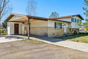 Tri-level home featuring driveway, brick siding, a carport, and a front yard