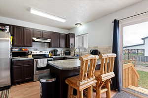 Kitchen with dark wood finish cabinets, stainless steel appliances, a kitchen breakfast bar, a peninsula, and light wood-style floors