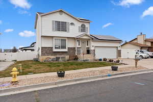 View of front facade with solar panels, a gate, brick siding, driveway, and an attached garage