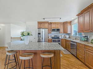 Kitchen with light stone counters, wood finish cabinets, stainless steel appliances, light wood finished floors, and recessed lighting