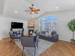 Living room with light wood-style flooring, a ceiling fan, a glass covered fireplace, and recessed lighting