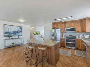 Kitchen featuring wood finish cabinetry, light stone counters, stainless steel appliances, and a center island