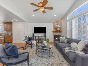 Living room with light wood-style flooring, lofted ceiling, a ceiling fan, a large fireplace, and recessed lighting
