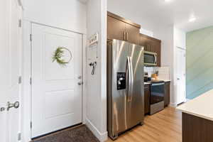 Kitchen with stainless steel appliances, light wood-style flooring, dark wood finish cabinetry, backsplash, and light stone countertops