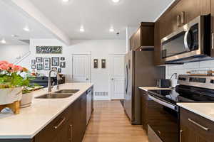 Kitchen with stainless steel appliances, dark wood finish cabinetry, light stone countertops, light wood-style flooring, and modern cabinets