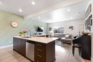 Kitchen with open floor plan, dark wood finish cabinets, stainless steel dishwasher, light wood-type flooring, and beamed ceiling