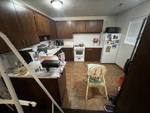 Kitchen featuring dark wood finish cabinets, light countertops, white appliances, a textured ceiling, and dark tile patterned flooring