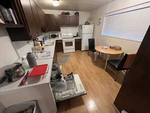 Kitchen with dark wood finish cabinetry, light wood-style flooring, white appliances, light countertops, and a textured ceiling