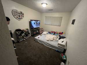 Carpeted bedroom featuring a textured wall and a textured ceiling